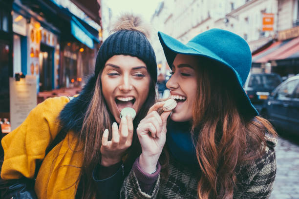 attraktive frauen essen pariser makronen - freunde imbiss großstadt stock-fotos und bilder