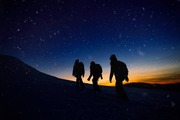 silhouette of three hiking friends moving up on the hill in cold winter day.
