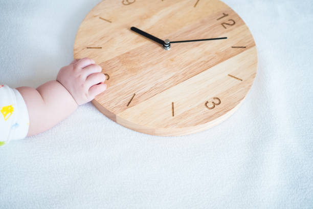 istock baby hand and wooden clock on blanket background 1050497916