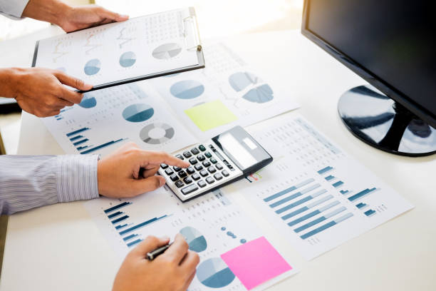istock Midsection Of Businessman Using Calculator While Colleague Holding Clipboard Table In Office 1050526226