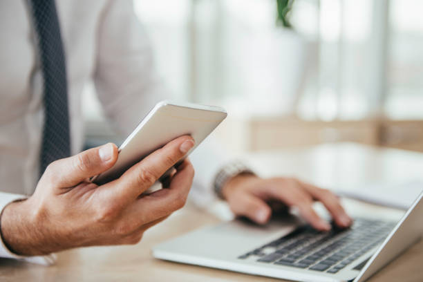 istock Midsection Of Businessman Using Laptop While Holding Mobile Phone On Table In Office 1050537316