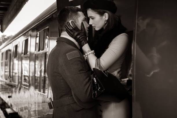 Vintage couple embracing on railway station platform as train is about to depart Vintage couple, handsome man in uniform, kissing goodbye his lover on railway station platform as train is about to leave. 1940s style stock pictures, royalty-free photos & images
