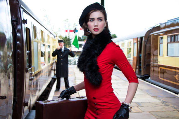 vintage attraente femmina che indossa abito rosso e berretto nero con valigie sulla piattaforma della stazione ferroviaria - 1940s style foto e immagini stock