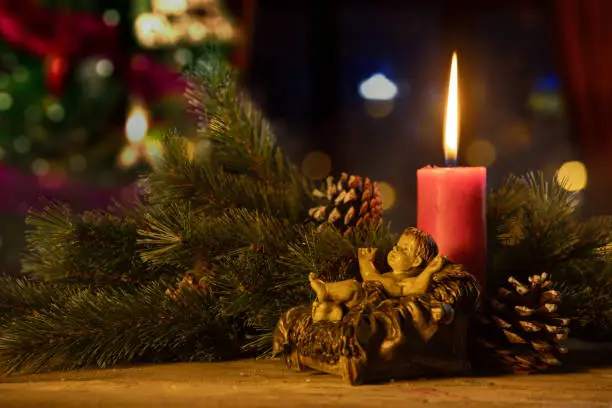 Twigs of the spruce with a baby Jesus statue and burning candle on blurred Christmas tree background