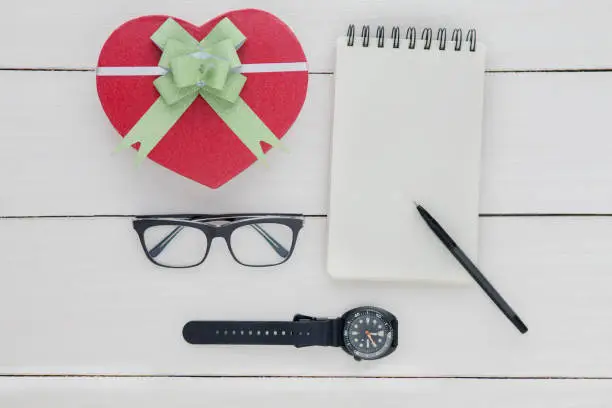 Father's day concept. Top view of blank paper notes, glasses, and wristwatch with a gift box shaped heart on the table