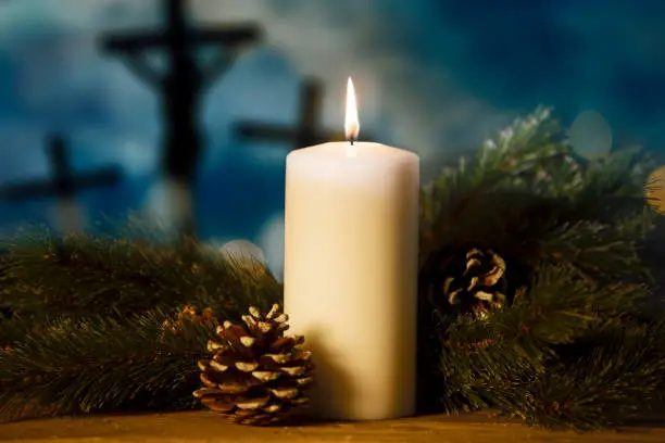 Close up of Christmas candle and pine branches on the table with blurred three crucifixes background