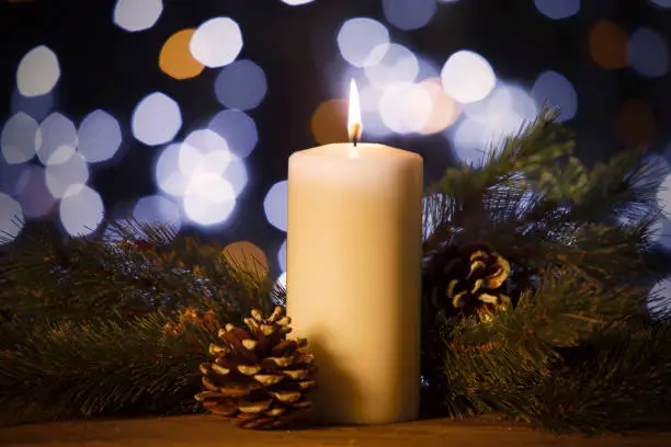 Closeup of Christmas candle with pine branches and pine cones on the wooden table with blurred sparkling light background