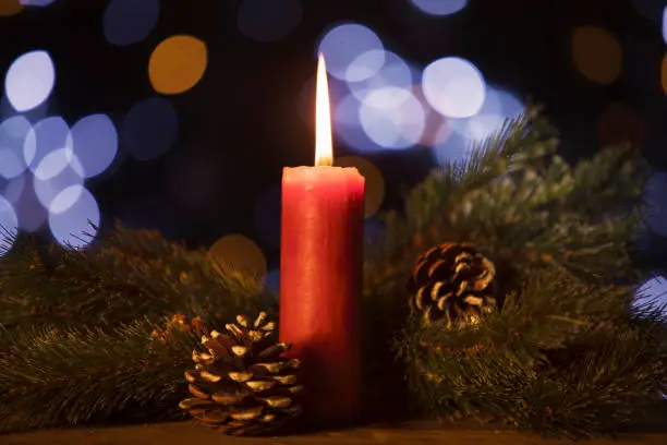 Image of Christmas candle with fir tree branches and cones on blurred twinkling light background