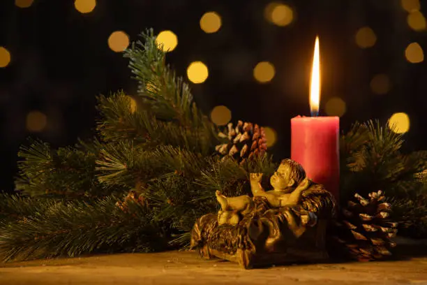 Christmas candle with a statuette of baby Jesus, pine cones, and fir branches. Shot with blurred lights
