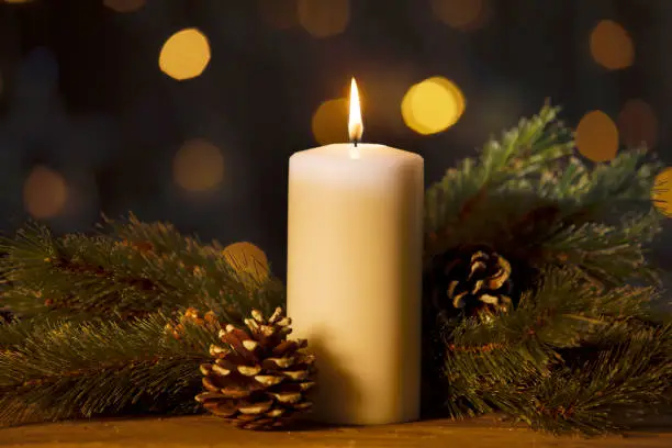 Christmas candle with branches and pine cones on the wooden table with blurred sparkling light background