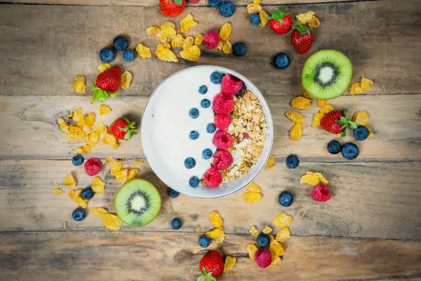 Top view of fresh berries with yogurt and cornflakes in a bowl. Shot on a wooden table