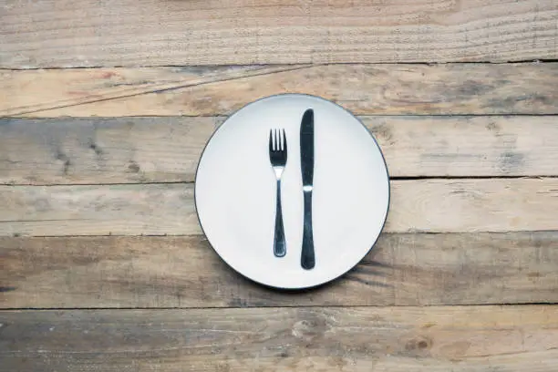 High angle view of a silver knife and fork on an empty plate with wooden table background