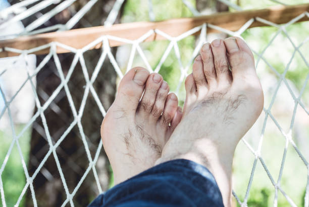 Close up of bare feet of a man resting in a hammock on a sunny day.