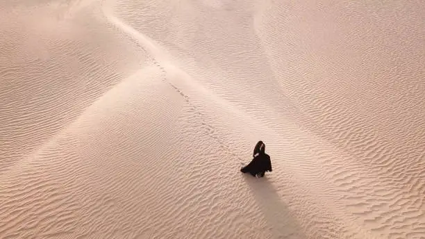 A woman in abaya (United Arab Emirates traditional dress) walking on the dunes in the desert during early morning at sunrise. Dubai, UAE.