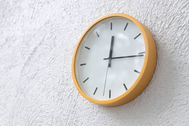 istock yellow clock on concrete wall show time  on mid day. 1050612664
