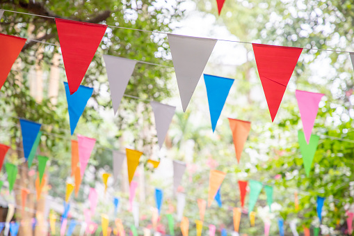colorful triangle flags hang on white rope in garden for decorative party.