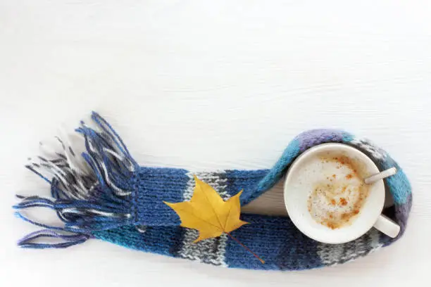 mug frothy cappuccino in blue scarf decorated with yellow maple leaf top view
