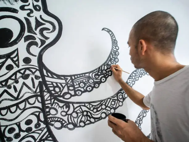 Photo of Closeup artist painting abstract pattern in octopus shape on white cement wall.