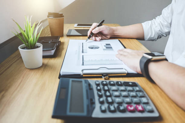 istock Businessman working on a graph document financial report and analysis calculation investment cost with calculator at office desk and other objects around 1050643376