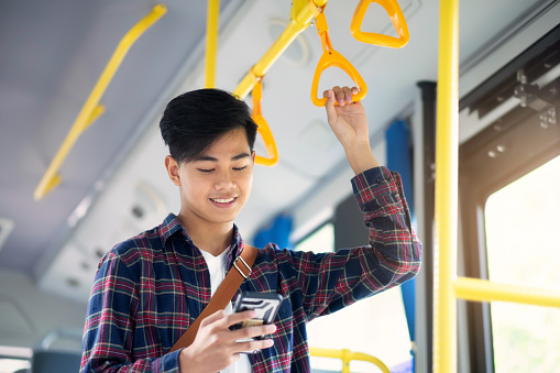 Young asian male passenger using mobile phone on public bus.