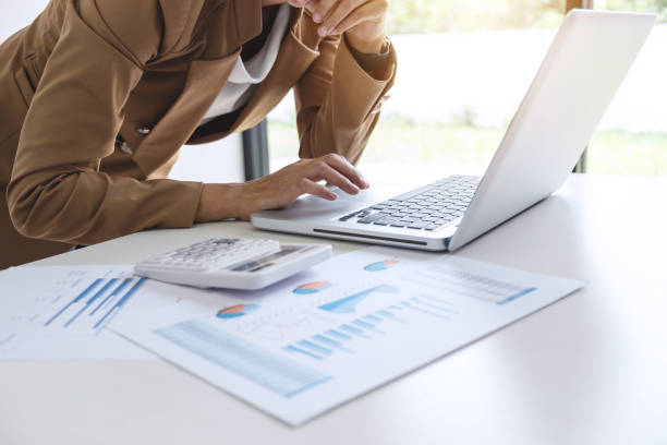 istock Elegant businesswoman leader working on laptop in a modern office, analyzing data and graph, using calculator calculate, young attractive woman typing on computer at white table 1050656818