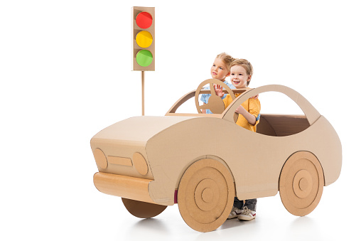 brother and sister playing with cardboard car and traffic lights, on white