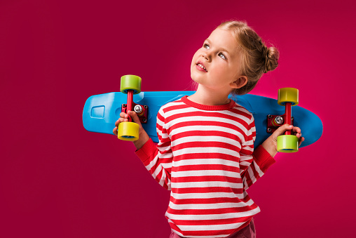 adorable stylish kid posing with penny board isolated on red