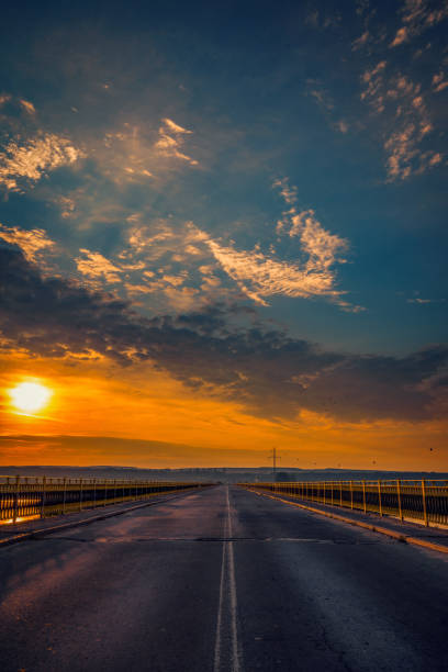 Metallic road bridge over a river at sunrise against a blue sky with clouds