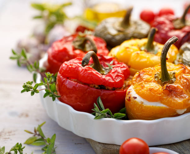 Roasted bell pepper with mushroom, rice, cheese and herbs filling in a baking dish on a white wooden table, close-up. Roasted bell pepper with mushroom, rice, cheese and herbs filling in a baking dish on a white wooden table, close-up. A healthy and delicious vegetarian food. stuffed pepper stock pictures, royalty-free photos & images