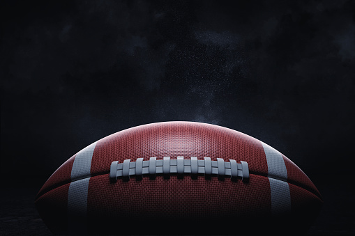3d rendering of a leather ball for American football lying with its seams in focus on a dark background. American national game. American football gear. Ball for professional sport.
