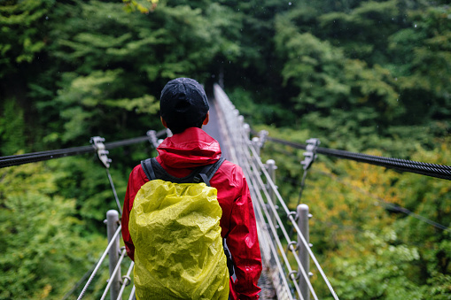 Mid adult man crossing a suspension bridge while hiking in a forest