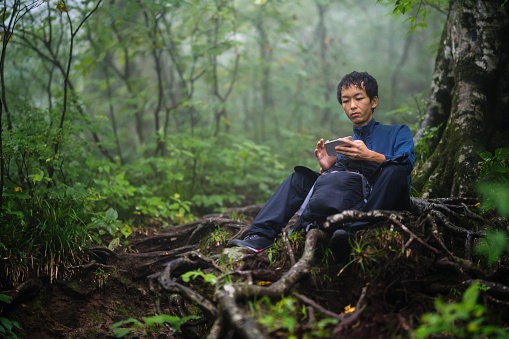 Mid adult man using a smartphone while hiking in a misty forest in Japan