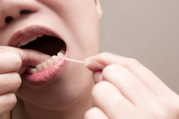 asian woman using dental floss to remove food and dental plaque from between teeth in areas a toothbrush is unable to reach - dental floss brushing teeth dental hygiene dental equipment imagens e fotografias de stock