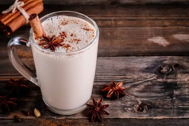 Homemade Chai Tea Latte with anise and cinnamon stick in glass mug on wooden rustic background