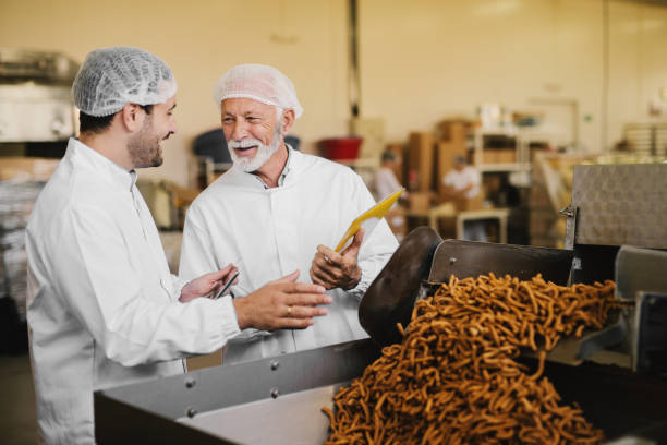 orgulloso padre y su hijo en ropa estéril en su fábrica de alimentos y comprobar la calidad de los productos. sonriente y manos gesticulando entre sí. - sales manager fotografías e imágenes de stock