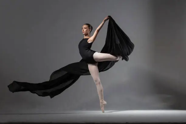 Graceful ballerina in black tights posing with black cloth. Studio photography. The concept of beauty and grace.