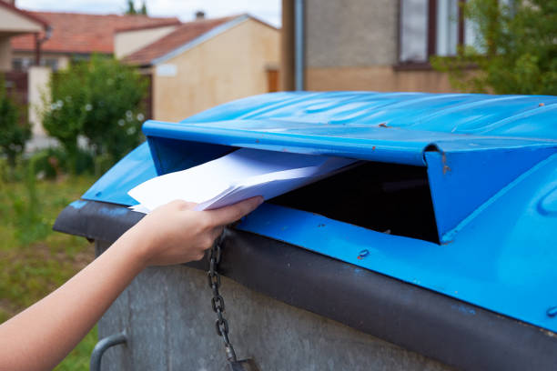 istock Young woman throwing paper documents into a blue container for sorted waste 1050726782