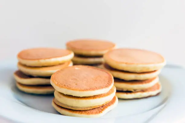 Pancakes on a white plate stacked on top of each other on a white background