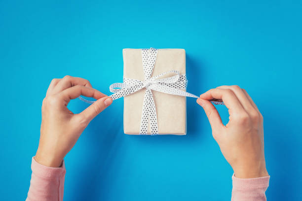 woman's hands untie bow on gift box on blue background, top view - hand wrap imagens e fotografias de stock