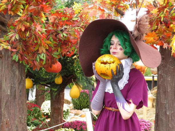 Girl cosplay character dressed as a witch with pumpkin in hands, Halloween concept Moscow, Russia - October 2018: Girl cosplayer dressed as a witch posing with pumpkin in hands on autumn decorations background during Moscow festival Golden Autumn. Harvest festival yellow fairy fan stock pictures, royalty-free photos & images