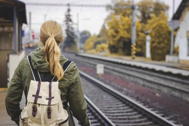 Photo of Woman with backpack standing at railroad station platform and waiting for a train. Travel concept.