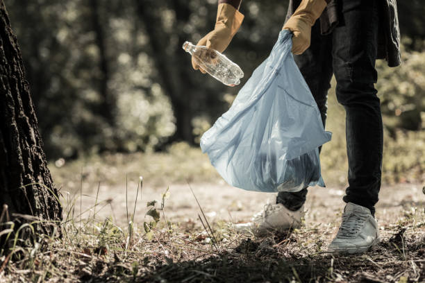 Young pupil wearing jeans and sneakers gathering empty bottles in the forest