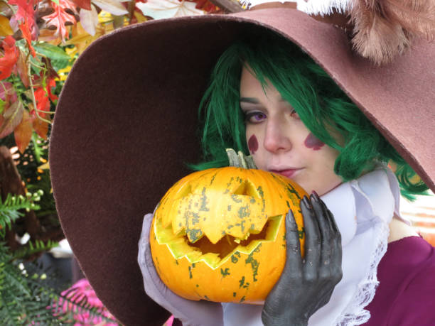 Cosplay girl with green hair dressed as a witch posing with pumpkin in hands. Halloween concept Moscow, Russia - October 2018: Cosplayer girl dressed as a witch posing with pumpkin in hands on autumn decorations background yellow fairy fan stock pictures, royalty-free photos & images