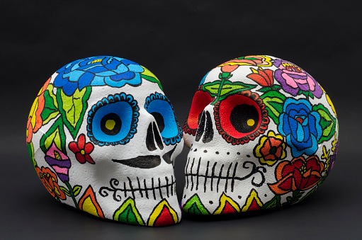 Hand painted styrofoam skulls with flowers against black background. Hand painted skulls for Halloween and mexican Day of the dead decoration