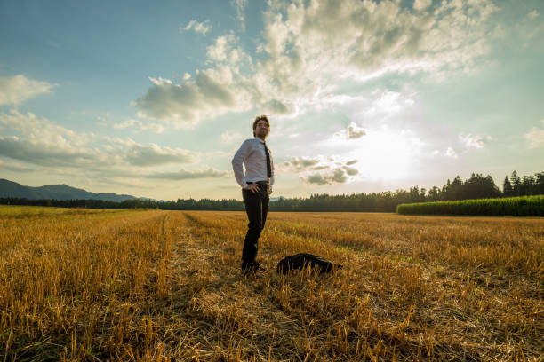 Young confident businessman standing in sawn field on a beautiful autumn evening under cloudy sky.