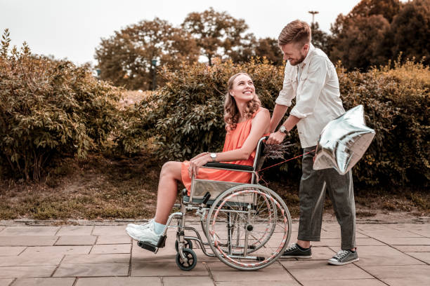 istock Kind man looking at his disabled girlfriend while pushing her wheelchair 1050820826