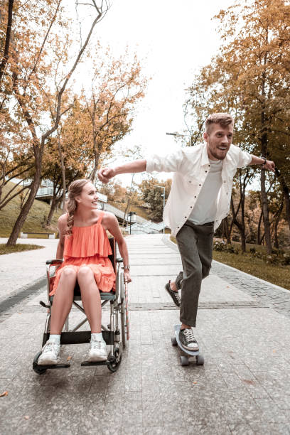 istock Enthusiastic man riding skateboard and disabled girlfriend looking at him 1050821136