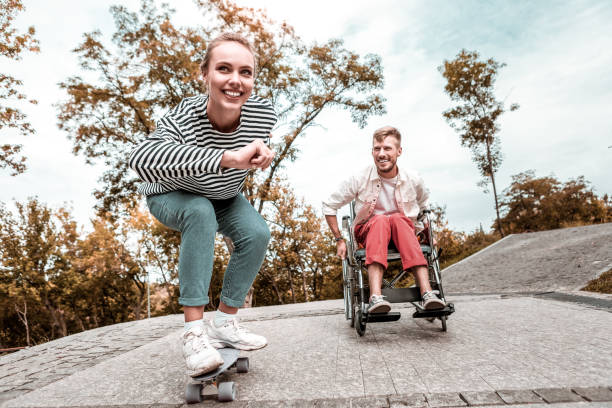 istock Active woman sitting and riding penny board while disabled man smiling 1050821896