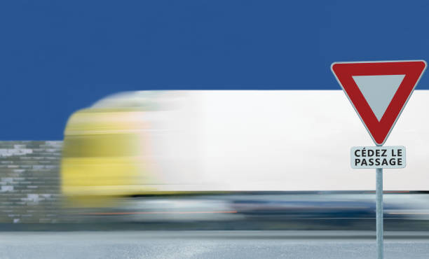 Give way yield french cédez le passage road sign, motion blurred truck vehicle traffic background, white signage triangle red frame regulatory warning, metallic pole post, blue summer sky, panneau signalisation cédez-le-passage, France dar cierto rendimiento muestra del camino francés cédez le paso, movimiento borrosa camión vehículo tráfico fondo, advertencia reglamentarios de señalización blanco triángulo marco rojo, post de poste metálico, azul cielo de verano, panneau señal