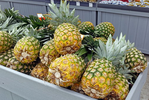 Sidewalk fruit market stand bin filled with fresh pineapples.
